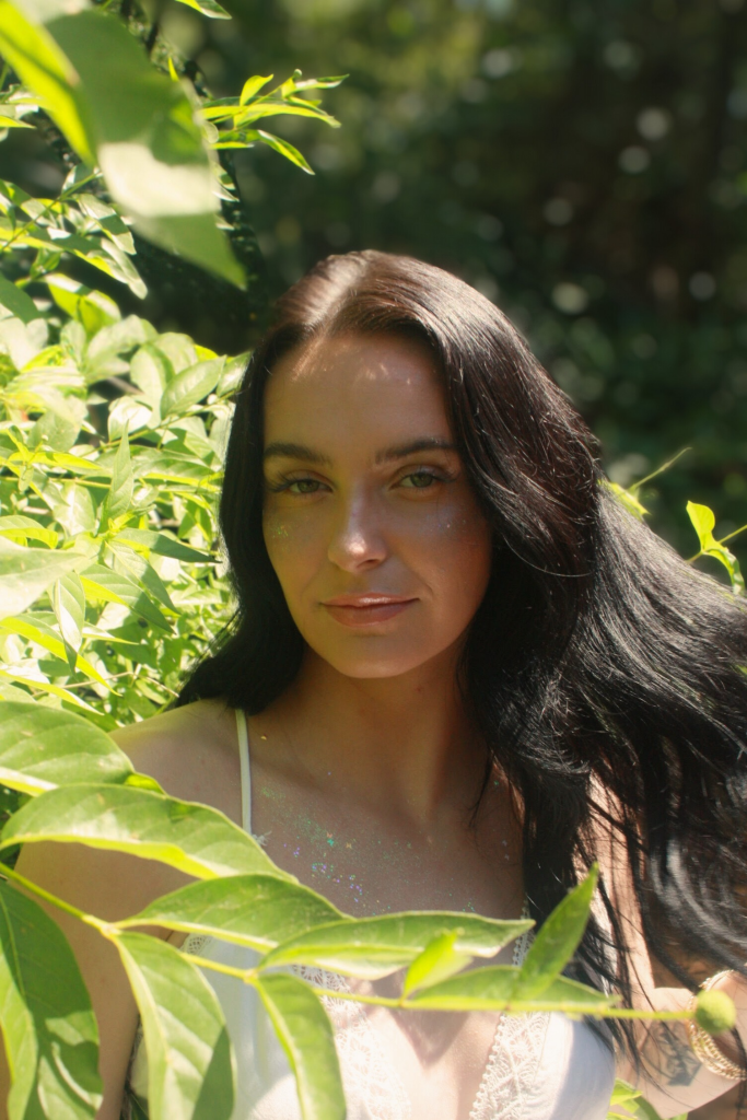 portrait of black haired woman with green leaves surrounding her