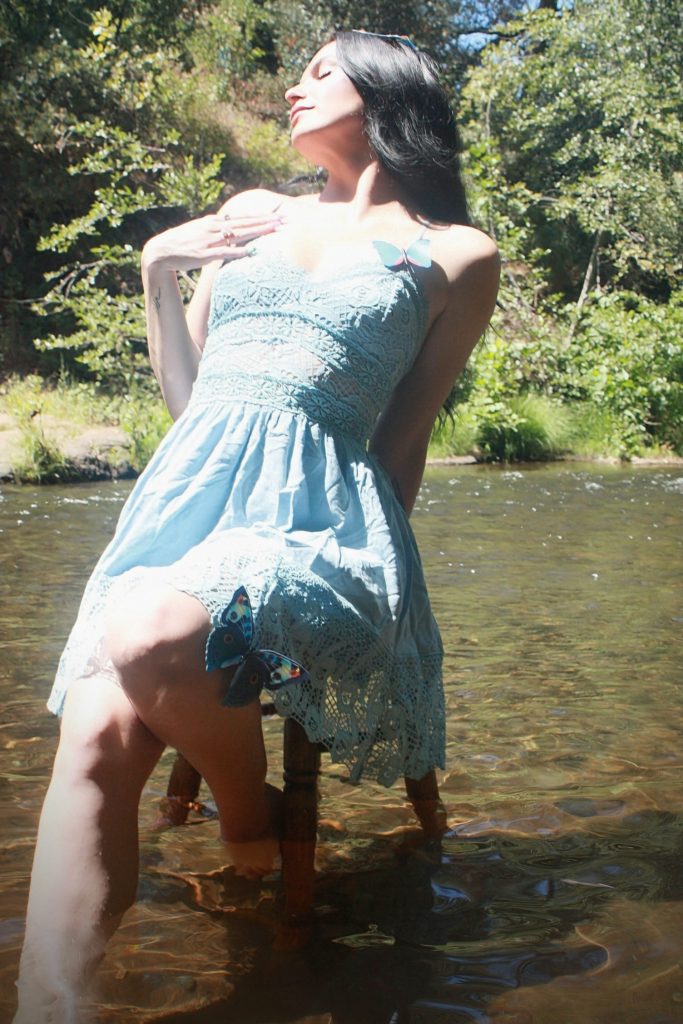brunette woman leaning back on a stool with her arm on her chest and feet in a river