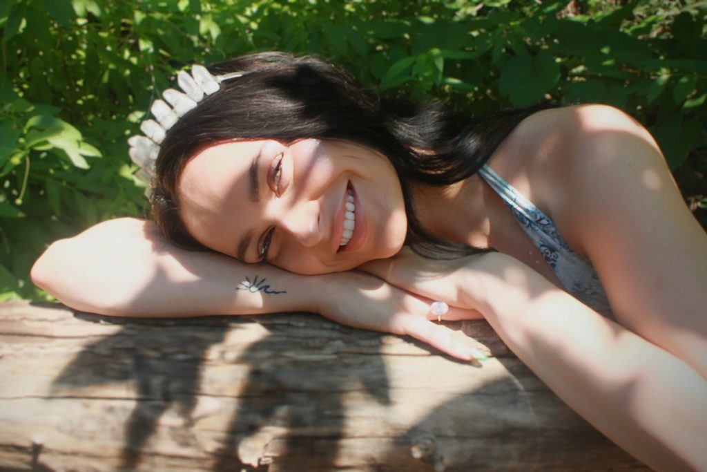 smiling woman resting her head on a log with sunshine and shadows on her face